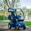 4 Wheel Mobility Scooter In Blue With Optional Solid Canopy Shown Outdoors.
